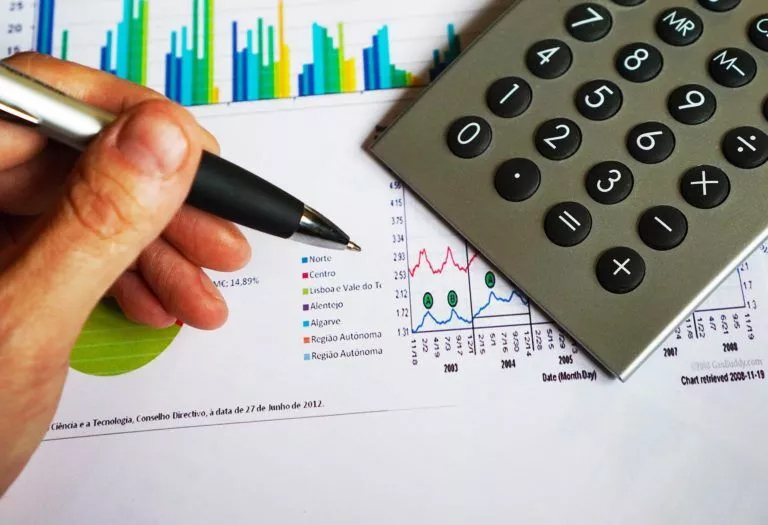 A student's hand holding a pen and calculator, seeking Accounting Homework Help