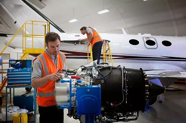 Two individuals, possibly aerospace engineering students, repairing an airplane engine in a hangar