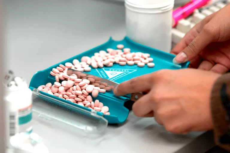 A person cutting pills into a blue tray, a task related to a Online Dispensing Help