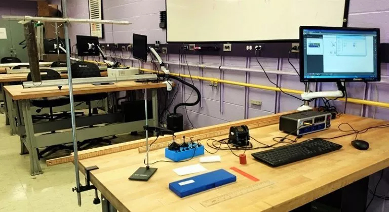 A classroom equipped with desks and computers on the wall, hosting a general physics homework help session 