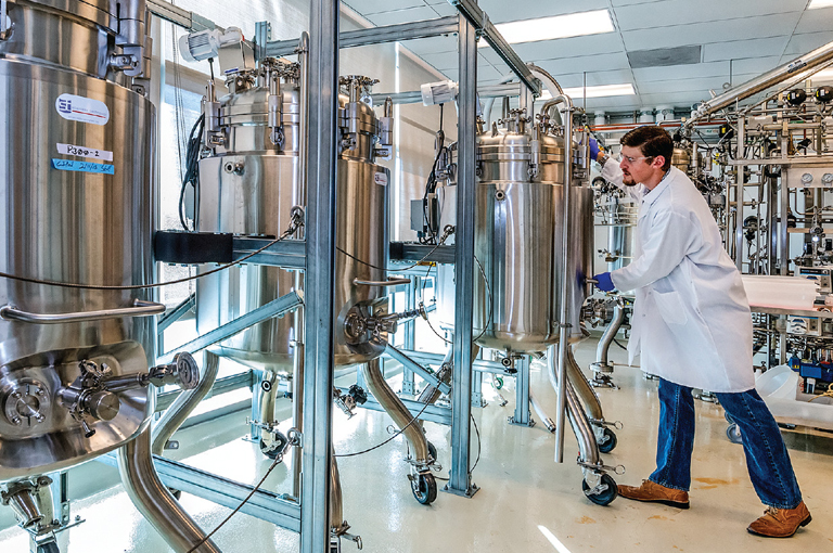 An image depicting a man in a lab coat standing in front of stainless steel tanks, representing industrial biotechnology assistance