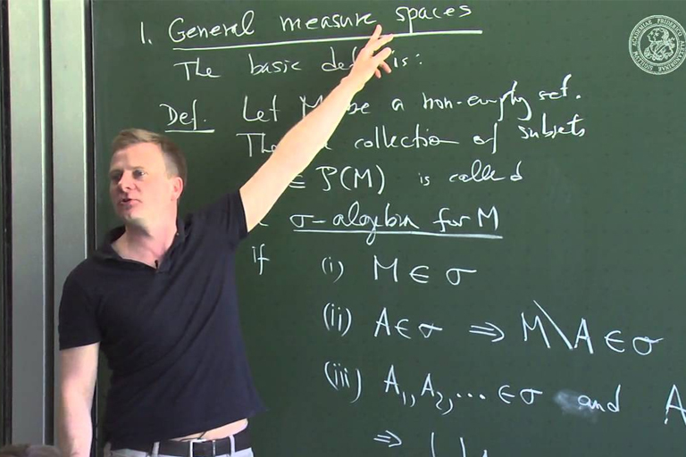 A tutor explaining measure theory concept on a blackboard with mathematical equations. Assisting with homework and assignments