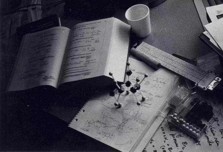 A monochrome image of a desk cluttered with papers and a cup representing organic chemistry homework help