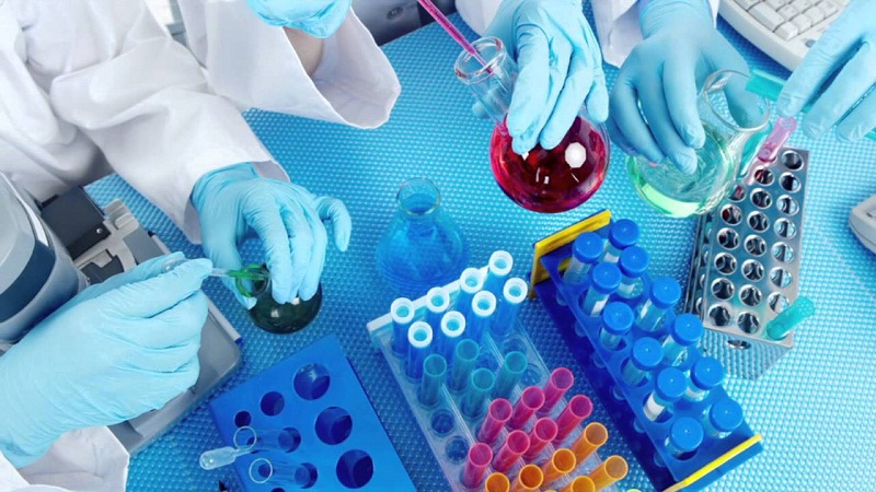 A group of students in lab coats and gloves working on a table they seem focused for getting pharmaceutical chemistry homework help