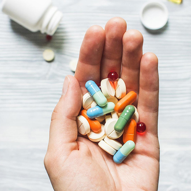 A person holds a variety of pills and capsules in their hand with a pill bottle in the background on a light-coloured surface, illustrating the complexities often faced when seeking pharmacology assignment help